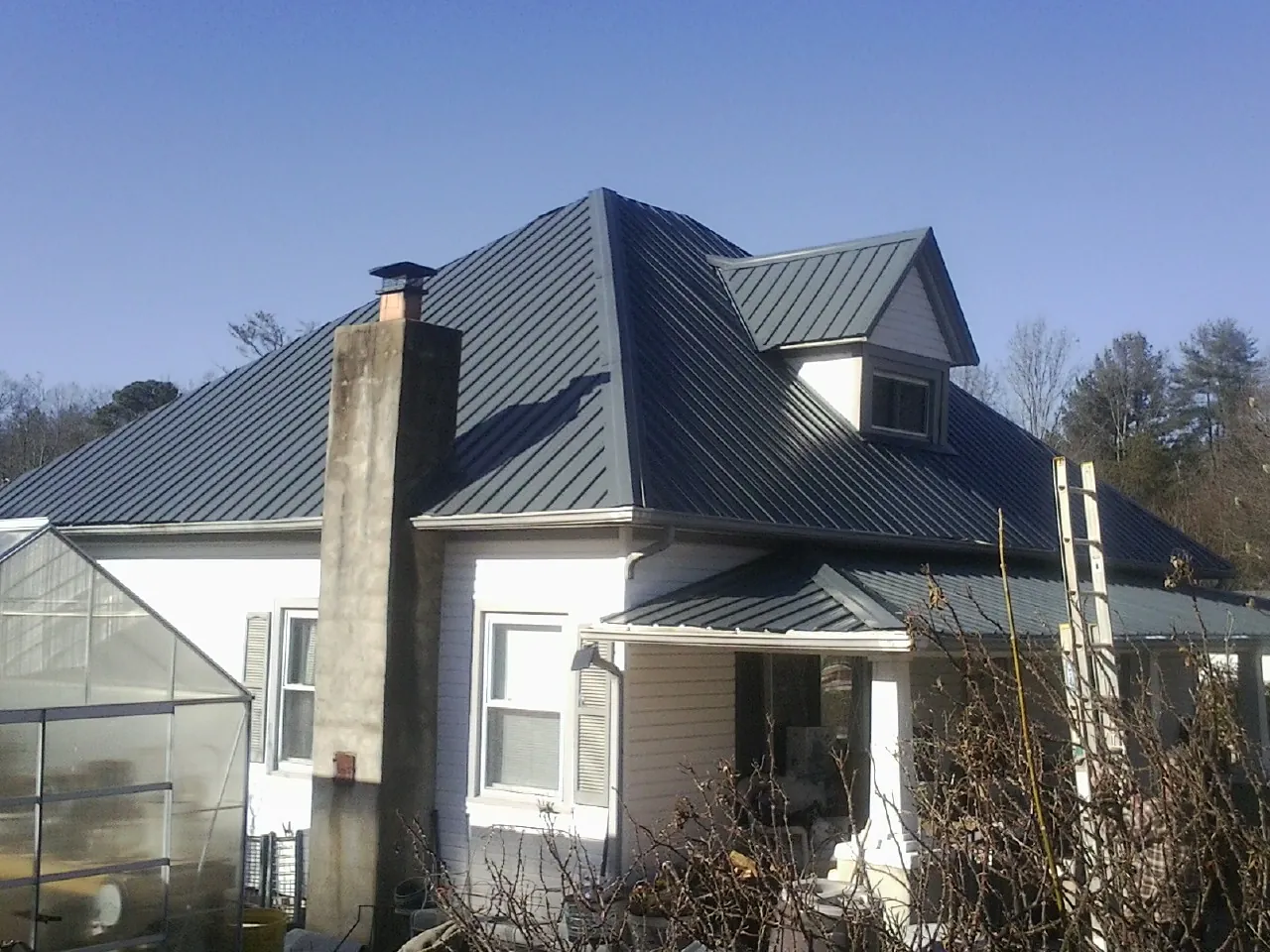 Dark blue standing seam metal roof on a white farmhouse with dormer — Slate & Tile Roof Repair by Roofing Brothers in Freeville