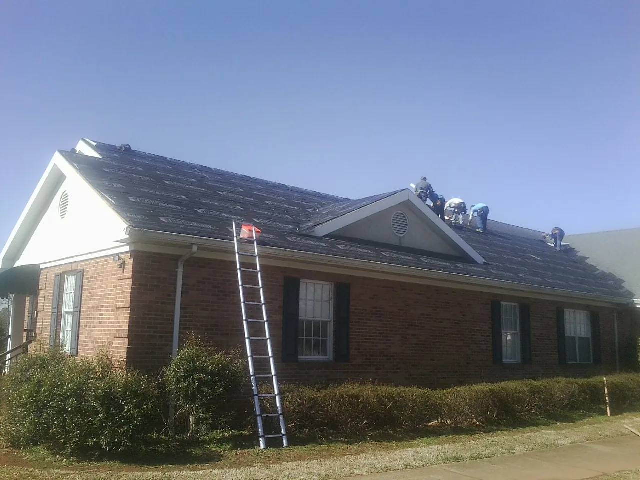 Crew tearing shingles off a brick ranch roof with a ladder set — Metal Roof Repair work by our crew in Freeville