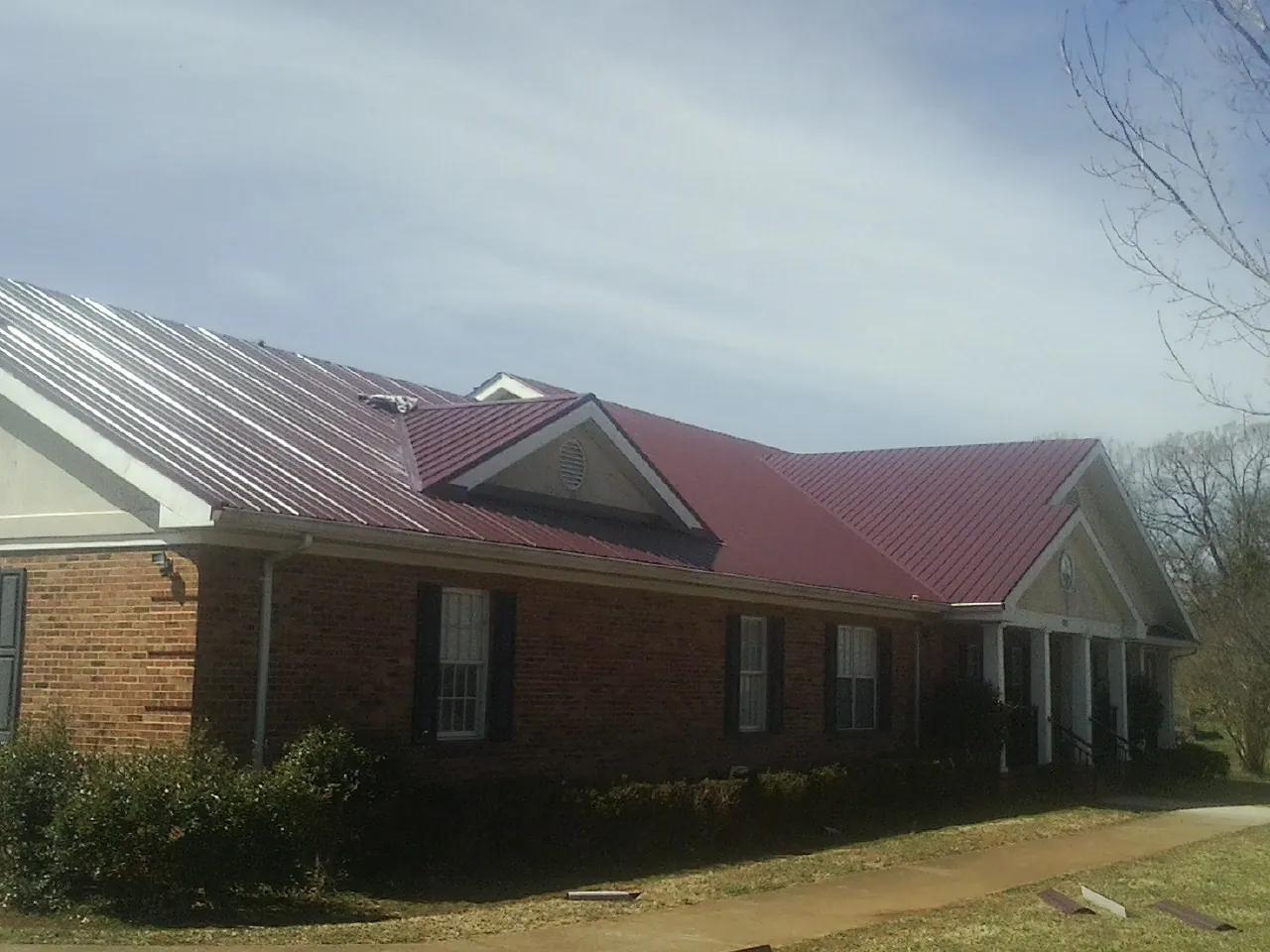 Red metal roof with gabled entries on a long brick building, from a Hail Damage Roof Repair job in Freeville