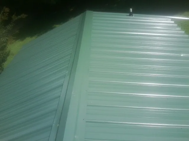 New green metal panels meeting at the ridge of a roof — Flat Roof Repair work by our crew in Freeville