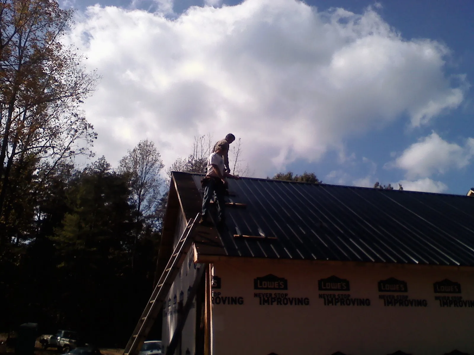 Roofer fastening dark metal panels high against a cloudy sky, from a Roof Inspection job in Freeville