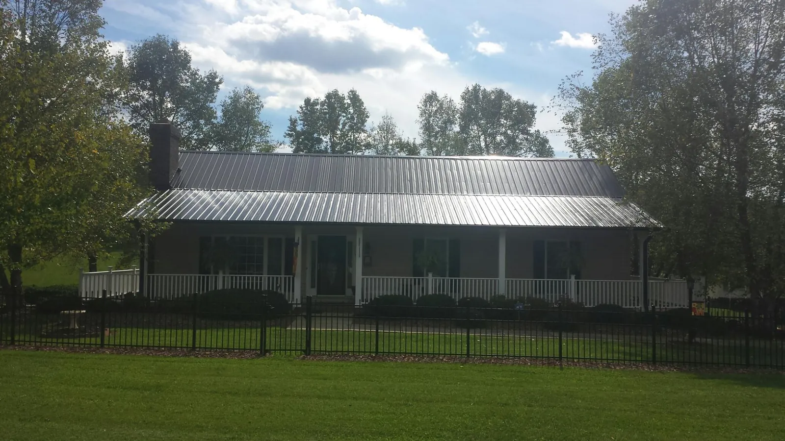 Gray metal roof on a brick ranch with a full width front porch — Gutter Guard Installation work by our crew in Freeville