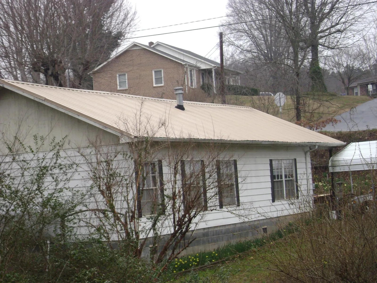 Tan metal roof on a white sided house set into a hillside — Commercial Roofing by Roofing Brothers in Freeville