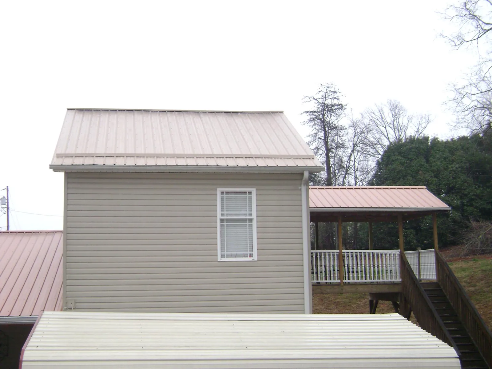 Tan metal roofs on a two story addition and attached porch, from a Roof Replacement job in Freeville